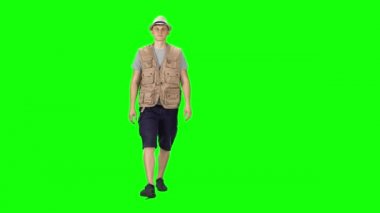 Young man in a grey t-shirt, sleeveless shirt, shorts, sneakers and hat going against a green background.