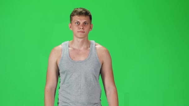 Young man in a grey singlet going and looking forward against a green background. Slow motion. — Wideo stockowe