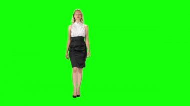 Blonde girl in black-white dress and high heel shoes going against a green screen.