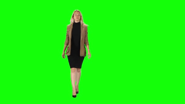Blonde girl in a stylish brown jacket, black dress and high-heeled shoes going against a green screen. — Stock video