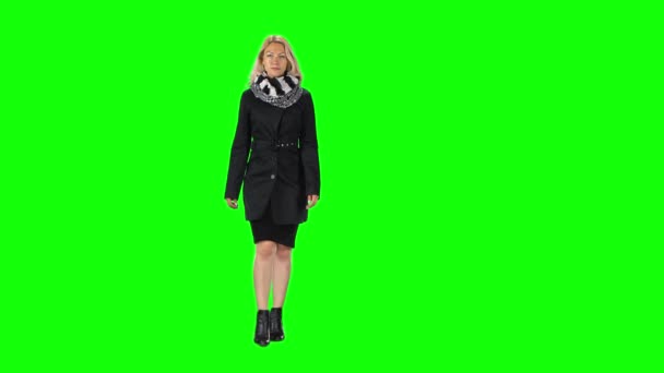 Blonde girl in a black dress, coat, scarf and boots going against a green screen. — Stock Video