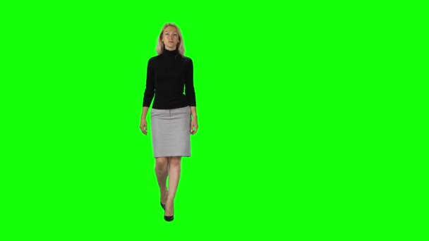 Blonde girl in black turtleneck, grey skirt and high heel shoes going against green screen. — Stok video