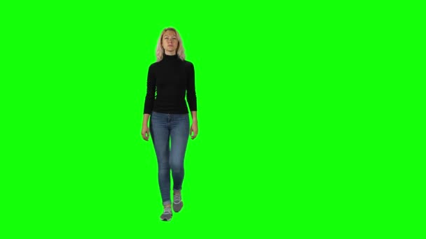 Blonde girl in black turtleneck, jeans and sneakers going against green screen. — ストック動画