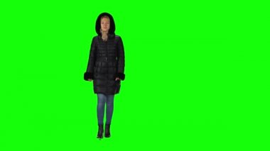 Blonde girl in a black winter coat with hood, jeans and boots going against a green screen.