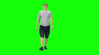 Young man in a grey t-shirt, shorts and sneakers going against a green background.
