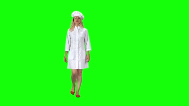 Blonde cook chef in white uniform and hat going against a green screen. — Stockvideo