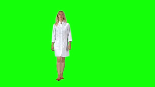 Blonde girl in a white medical coat going against a green screen. — Stock video