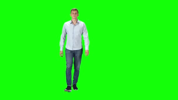 Young man in a gray shirt, jeans and sneakers going against a green background. — Stock Video