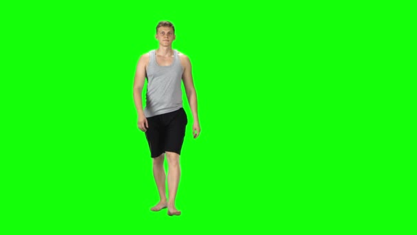 Молодой человек в сером сингле и шортах идет на зеленом фоне . — стоковое видео