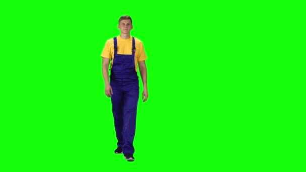 Young man in uniform, yellow t-shirt and blue jumpsuit going against green background. — Stock Video