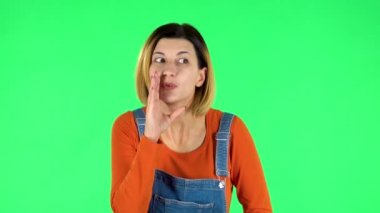 Girl looks around, covers her mouth with her hand and whispers the secret and making a hush gesture. Green screen