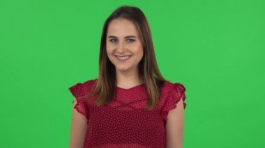 Portrait of tender girl in red dress is coquettishly smiling while looking at camera. Green screen