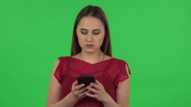 Portrait of tender girl in red dress is texting on her phone. Green screen