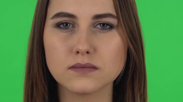 Woman is looking straight and blinking on green screen. Close up — ストック動画