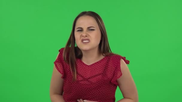 Portrait of tender girl in red dress is feeling very bad, her stomach hurting. Green screen — Stock video