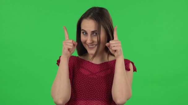 Portrait of tender girl in red dress is pointing up fingers. Green screen — 图库视频影像