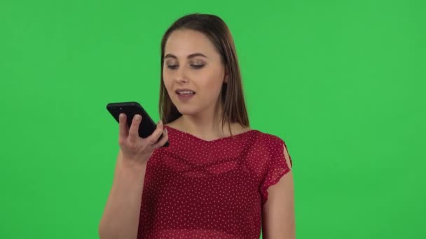 Portrait of tender girl in red dress is asking for information on the network via phone. Green screen — Stockvideo