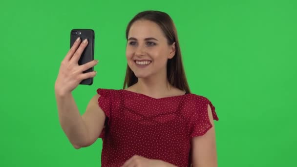 Retrato de menina macia em vestido vermelho está falando por vídeo chat usando telefone celular e se alegrar. Tela verde — Vídeo de Stock