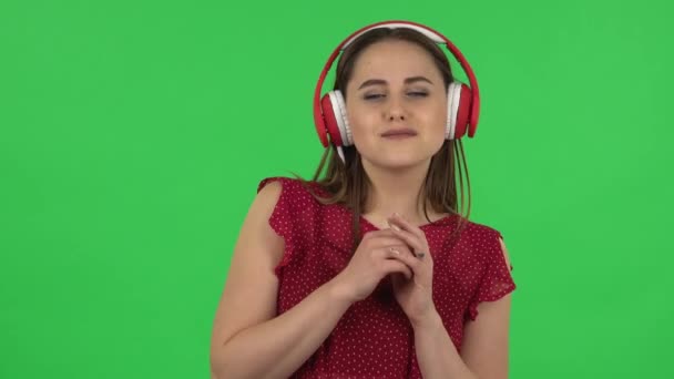 Portrait de tendre fille en robe rouge danse et profiter de la musique dans les grands écouteurs rouges. Écran vert — Video