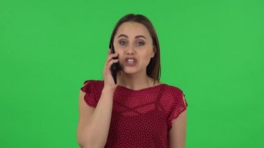 Portrait of tender girl in red dress is talking for mobile and shocked then rejoice. Green screen