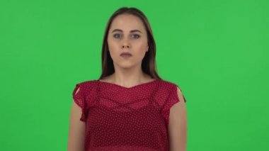 Portrait of tender girl in red dress carefully examines something then fearfully covers her face with her hand. Green screen