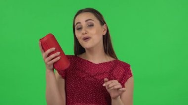 Portrait of tender girl in red dress is listening to music with bluetooth portable speaker and dancing. Green screen