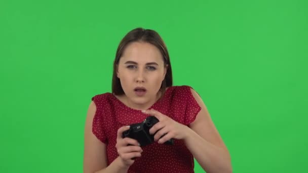 Retrato de tierna chica en vestido rojo está jugando un videojuego usando un controlador inalámbrico y perdiendo. Pantalla verde — Vídeos de Stock