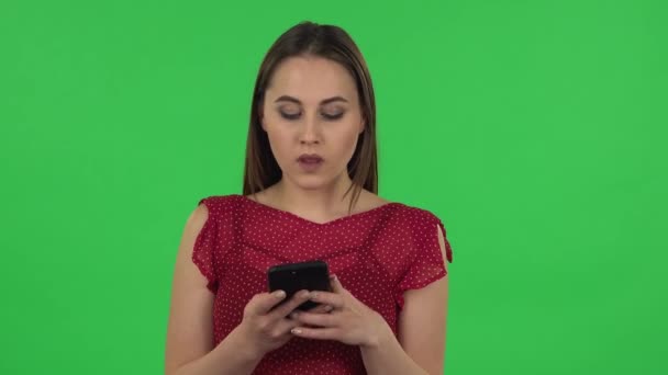 Retrato de menina feliz concurso em vestido vermelho está enviando mensagens de texto em seu telefone. Tela verde — Vídeo de Stock