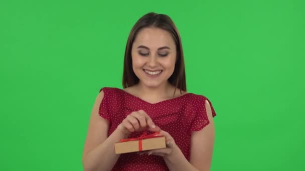 Portrait of tender girl in red dress is opening the gift, very surprised and upset. Green screen — Αρχείο Βίντεο