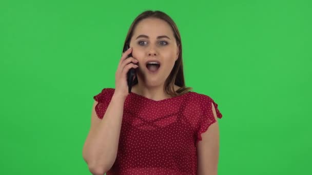 Portrait of tender girl in red dress is talking for mobile and shocked then rejoice. Green screen — Stockvideo