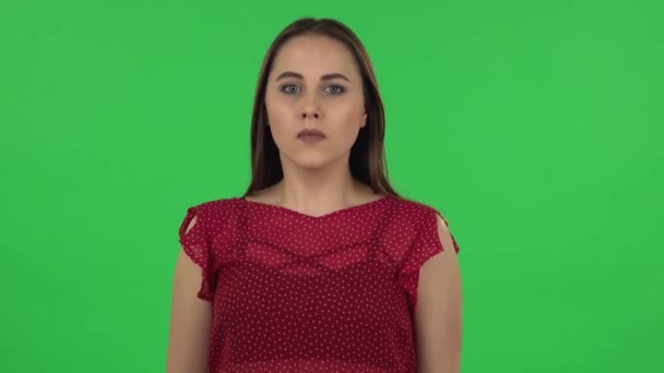 Портрет нежной девушки в красном платье тщательно исследует что-то, а затем страшно закрывает лицо рукой. Зеленый экран — стоковое видео
