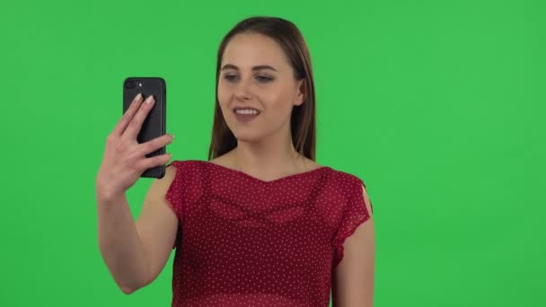 Portrait of tender girl in red dress is talking for video chat using mobile phone and dissatisfied. Green screen — Stockvideo