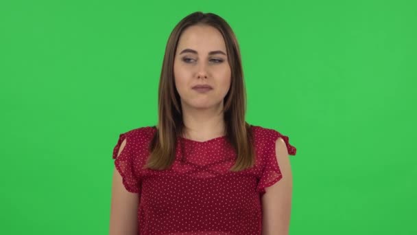 Portrait of tender confused girl in red dress is saying oops and shrugging. Green screen — Stockvideo