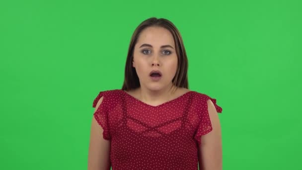 Портрет нежной девушки в красном платье слушает информацию, шокированную и очень расстроенную. Зеленый экран — стоковое видео