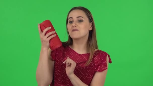 Portrait of tender girl in red dress is listening to music with bluetooth portable speaker and dancing. Green screen — Stok video