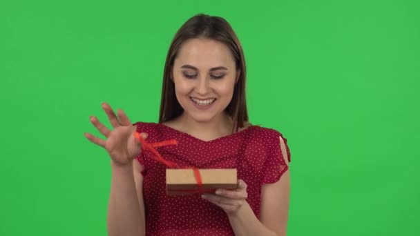 Portrait of tender girl in red dress is opening the gift, very surprised and rejoicing. Green screen — Stockvideo