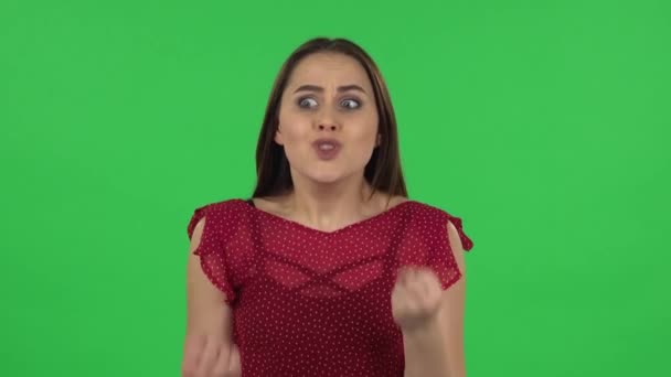 Portrait of tender girl in red dress is upset, waving her hands in indignation, shrugging. Green screen — ストック動画