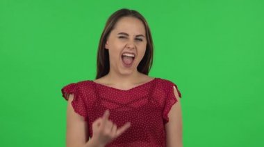 Portrait of tender girl in red dress is making a rock gesture and enjoying life. Green screen