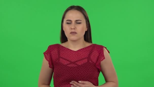 Portrait of tender girl in red dress is feeling very bad, her stomach hurting, feeling nausea. Green screen — ストック動画