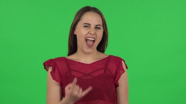 Portrait of tender girl in red dress is making a rock gesture and enjoying life. Green screen — ストック動画