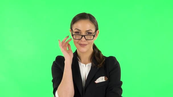 Portrait of brunette girl in bussines suit fixing her glasses, raising eyebrow and winks with smiling at green screen — Stok video