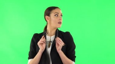 Charming girl takes off glasses, looks around, covers her mouth with her hand and whispers the secret. Green screen