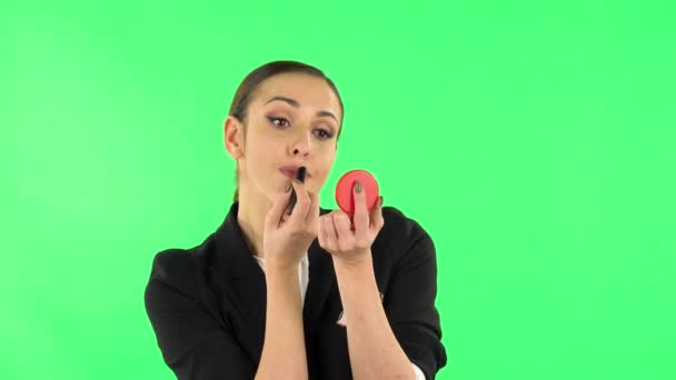 Het meisje schildert haar lippen terwijl ze in een rode spiegel kijkt. Groen scherm — Stockvideo