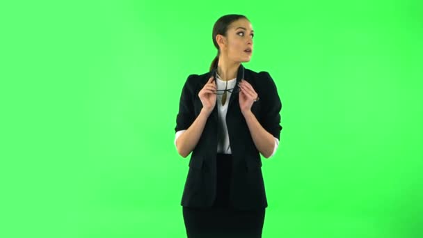 Charming girl takes off glasses, looks around, covers her mouth with her hand and whispers the secret. Green screen — Stock video