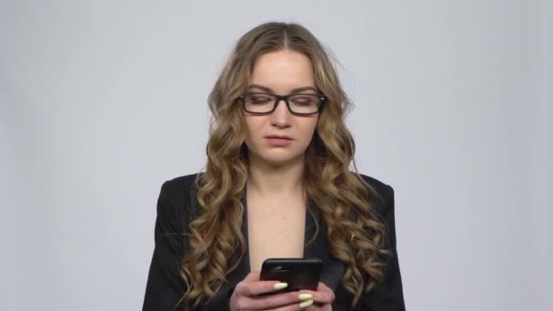 Wściekła bizneswoman smsuje na telefonie na szarym tle w studio — Wideo stockowe