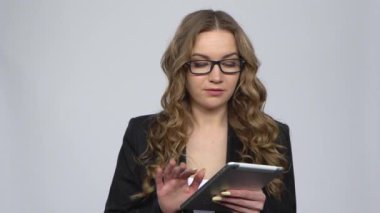 Stüdyoda gri arka plan üzerine tabletine mesaj atan düşünceli bir kadın.