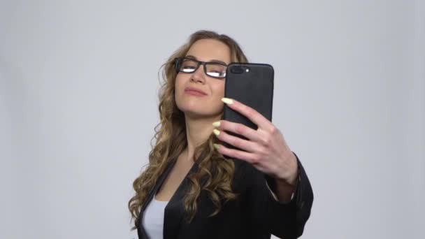 Hezká dívka dělá selfie na mobilním telefonu a pak hledá fotografie na šedém pozadí ve studiu