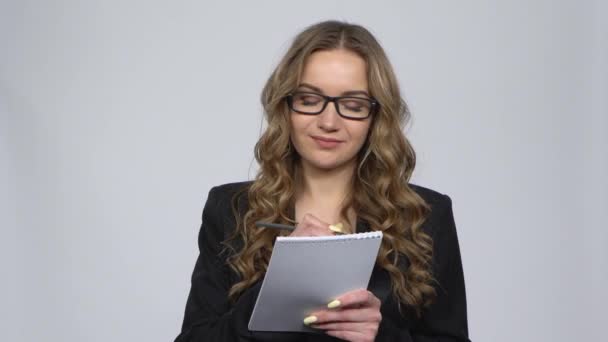 Mujer en un traje de negocios escribe en un cuaderno y luego nerviosamente arrancando una página sobre un fondo gris en el estudio — Vídeo de stock