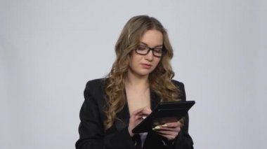 Kadın ofis çalışanı stüdyodaki gri arkaplan üzerinde hesap makinesi üzerinde hesaplamalar yapıyor.