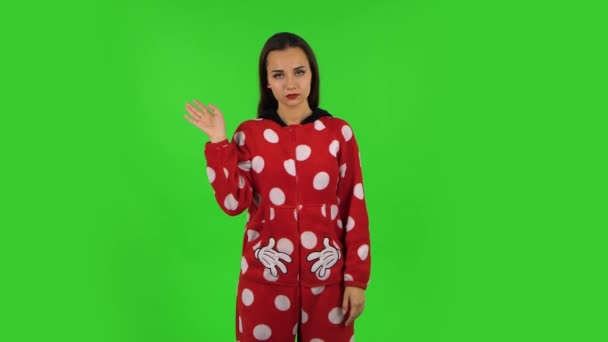 Красивая девушка в пижаме из красного руна машет рукой и показывает жест сюда. Зеленый экран — стоковое видео